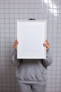 anonymous person covering face with empty white photo frame